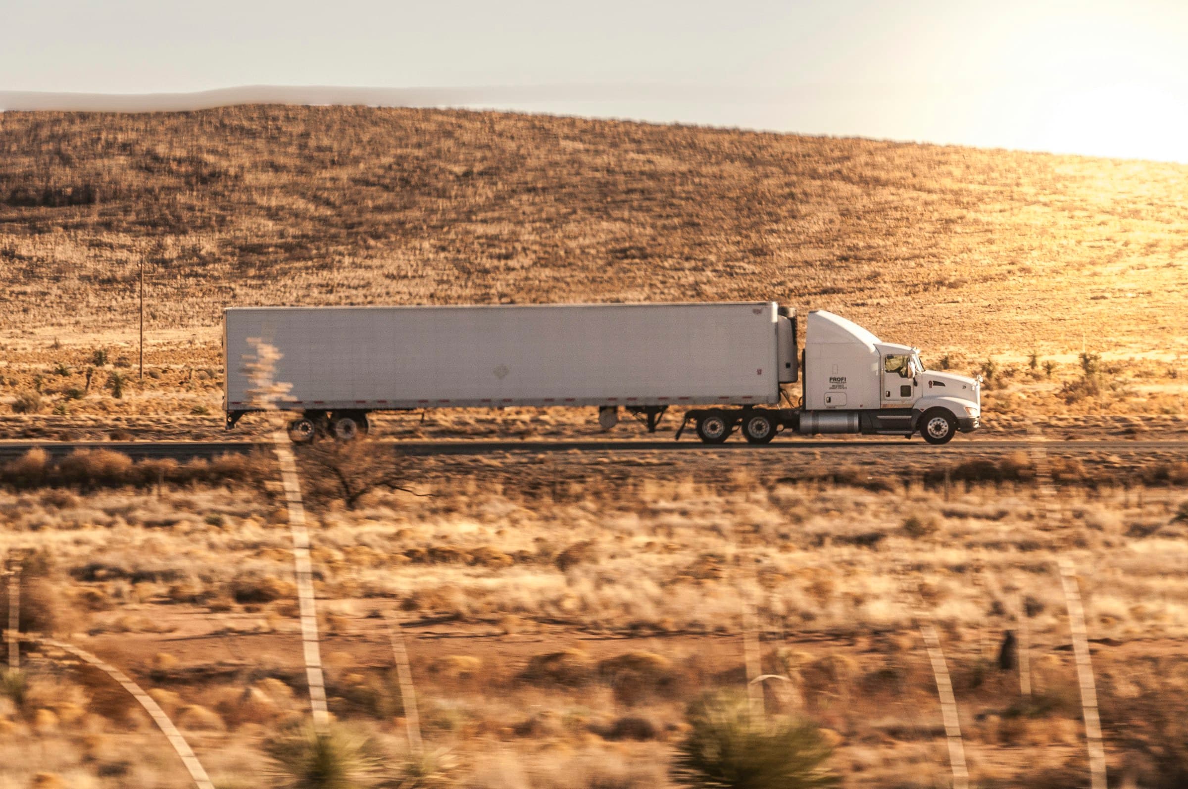 A white Clelland semi-truck travelling through golden desert grassland